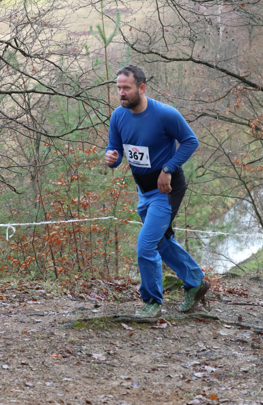 A runner climbs a rocky trail in a winter forest.